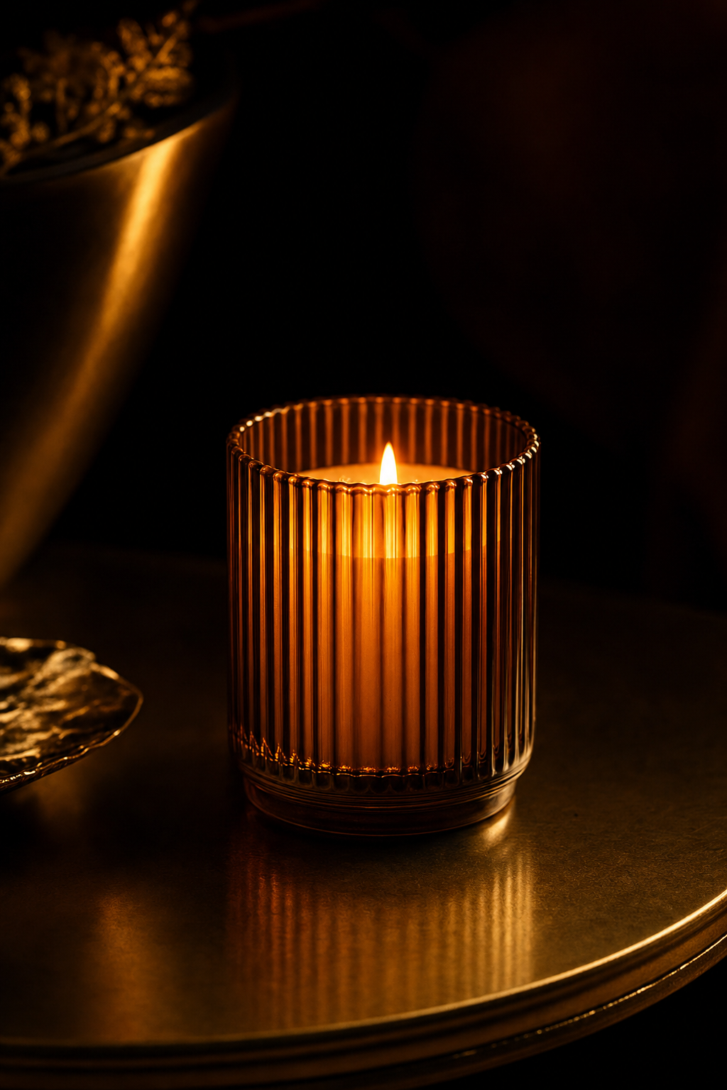 Amber ribbed glass candle glowing on a bronze surface